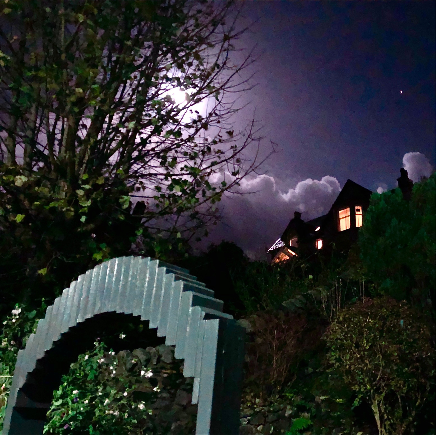 spooky house on a spooky hill with a spooky moon behind some spooky clouds lighting a big spooky tree